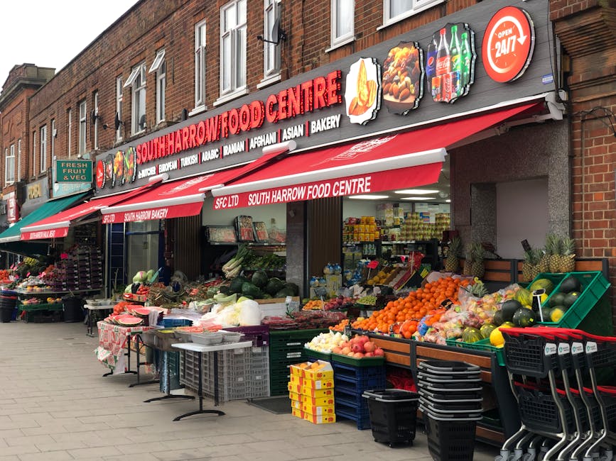 Exterior view of South Harrow Food Centre, a grocery store situated on a brick building street. The store has a prominent red and white awning displaying the store's name, with signs indicating fresh 